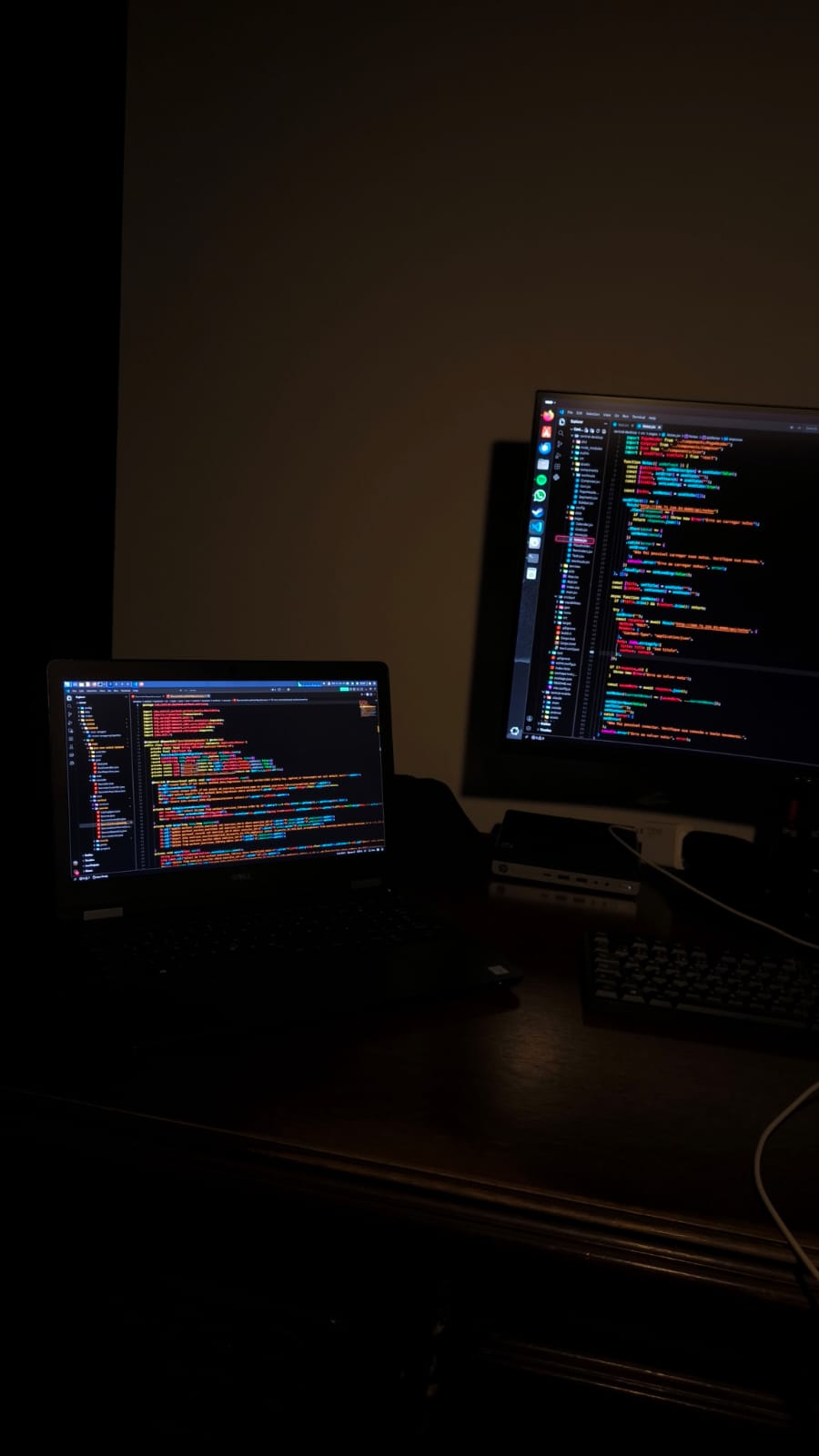 Mesa de trabalho com notebook e monitor exibindo código